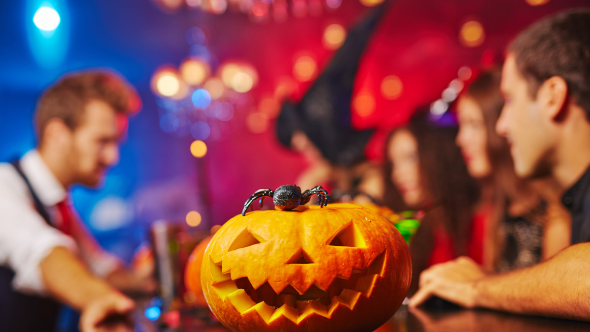 Wydrążona dynia na stole i uczestnicy imprezy w halloweenowych przebraniach